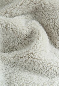 Cream-colored plush blanket with soft, textured surface. Fuzzy fibers create a cozy appearance, featuring a wavy, layered design.