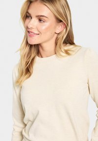 Svetlo bež pleteni pulover z rebrastim krojem, ki ima gladko teksturo in oprijete rokave. Minimalističen dizajn brez vzorcev ali dodatkov.
