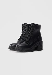 Zwarte leren enkelboots met een hoge stevige hak, vetersluiting aan de voorkant, gewatteerde kraag en ribbelige zool. Gladde textuur en minimale details.