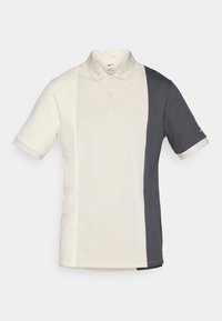 Nike polo majica s razdvojenim dizajnom, bijela s lijeve strane i tamnosiva s desne strane, kratki rukavi i klasični ovratnik.