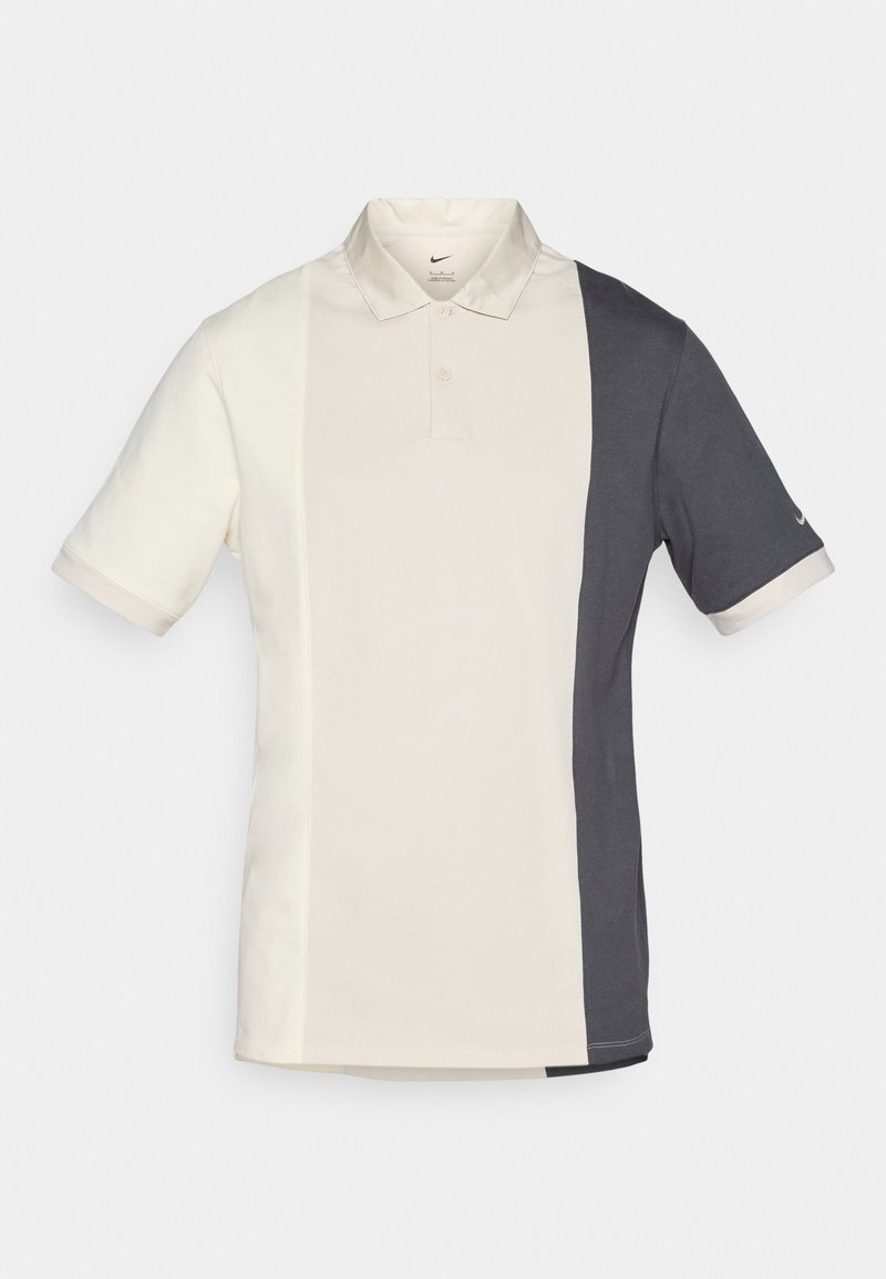 Camisa polo de Nike con un diseño dividido, blanca a la izquierda y gris oscuro a la derecha, de manga corta y con un cuello clásico.