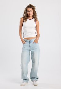 White sleeveless top with burgundy trim, paired with light blue loose-fit jeans and white sneakers. Straight leg design, casual style.