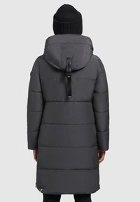 Gray puffer coat with a hood, featuring a vertical logo strap, quilted design, and zippered side vents. Knitted black beanie completes the look.
