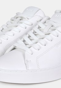 Sneakers bianchi in pelle con lacci piatti, punta arrotondata e dettagli cuciti. Texture liscia e branding minimo sulla linguetta.