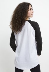 Svart och vit raglantröja med långa ärmar, med en böjd nederkant och en mjuk bomullstextur. Synliga sömmar på ärmarna.