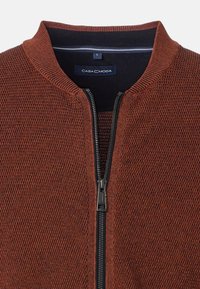 Texturerad rostfärgad zip-jacket med ribbat krage och kontrasterande marinblå innertyg. Har en robust svart dragkedja och en avslappnad design.