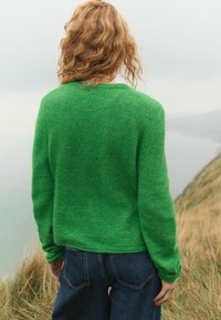 Groene wollen trui met een ontspannen pasvorm, ronde halslijn en lange mouwen, gecombineerd met hoogwaist donkerblauwe jeans. Gestructureerde afwerking.