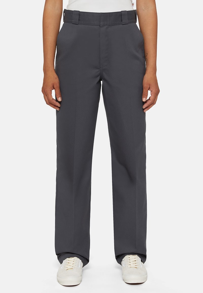 Pantalon gris à jambes larges avec une taille ajustée, des plis avant et une texture lisse ; porté avec des baskets blanches pour le contraste.