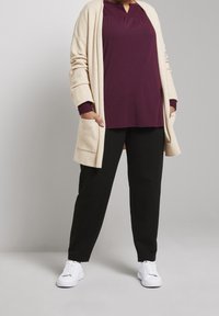 Lys beige lang cardigan, lilla top med plisseret halsudskæring, sorte bukser og hvide sneakers. Har lommer og afslappet pasform.