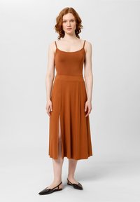 Robe marron sans manches avec un corsage ajusté et une jupe fluide présentant une fente sur le côté. Tissu doux avec une texture lisse, longueur cheville.