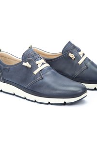 Námořnické kožené boty s hladkým povrchem, mají béžové tkaničky a bílou gumovou podrážku. Prodyšné detaily na bocích.