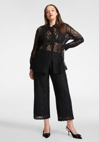 Czarna koronkowa bluzka z długimi rękawami i zapinana na guziki, zestawiona z czarnymi, koronkowymi spodniami o szerokich nogawkach, ozdobionymi falistymi wykończeniami i fakturami.