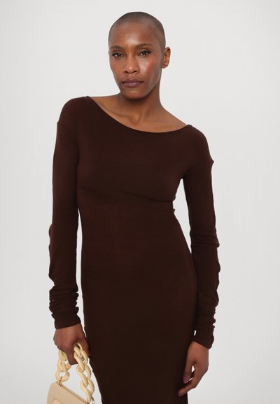 Bruine lange mouw jurk met een aansluitend ontwerp en een off-shoulder halslijn. Houdt een crèmekleurige gestructureerde tas vast met een gevlochten band.