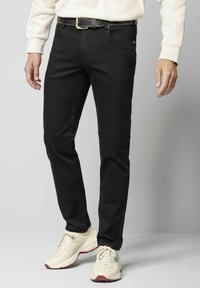 Jeans en denim noir avec une coupe slim, dotés d'un design classique à cinq poches et d'accents cousus. Portés avec des baskets blanches.