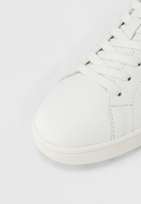 Λευκό δερμάτινο αθλητικό παπούτσι με στρογγυλεμένη μύτη, επίπεδα κορδόνια και διακριτικές ραφές. Ομαλή υφή και μινιμα λιστικός σχεδιασμός.