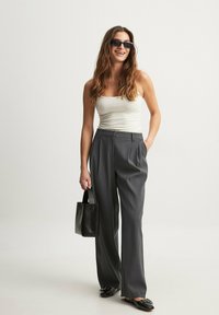 Pelēki plaša kāju bikses no gludas auduma, apvienotas ar pieguļošu baltu topu un melniem aksesuāriem, tostarp strukturētu rokassomu un saulesbrillēm.