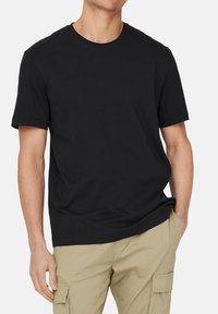 Sort bomulds T-shirt med klassisk rund halsudskæring og korte ærmer, der har en afslappet pasform og glat tekstur. Bæres med beige cargo bukser.