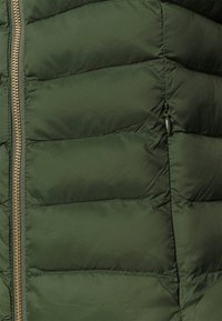 Olivgrön puffjacka med horisontell sömnad, guldzipper och en sidoficka. Slät, vattenavvisande tygtextur.
