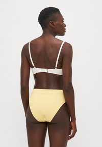 Ensemble de bikini comprenant un bralette texturé blanc avec des bretelles réglables et un bas taille haute jaune, complété par une fermeture à clip.