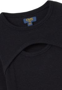 Schwarzes, gerippter Kinderoberteil mit rundem Ausschnitt und einem kreisförmigen Ausschnitt-Detail auf der Vorderseite, mit einem Markenetikett im Inneren.