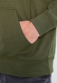 Felpa verde oliva con tasca a marsupio, polsini e orlo a costine. Tessuto morbido, design casual con dettagli di cucitura minimi.