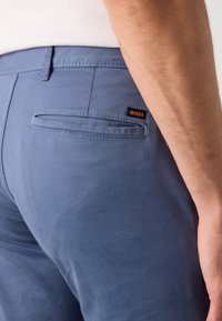 Pantalons en coton bleu avec une coupe slim, dotés d'une poche arrière et d'une petite étiquette orange "BOSS". Texture lisse et design ajusté.