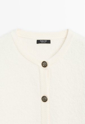 Cardigan bianco lavorato a maglia con scollatura rotonda, caratterizzato da un motivo a rilievo e un bottone dorato con un emblema di leone al centro.