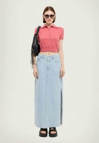 Ružový krátky polo tričko, svetlomodrá dlhá denimová sukňa s bočným rozparkom, čierna kabelka s třásňami a robustné čierne sandále.