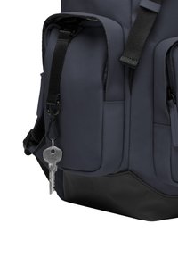 Sac à dos bleu marine en tissu texturé, comportant plusieurs poches et une base noire, avec une clé attachée par un clip sur le côté.