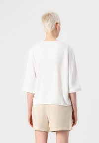 White, lightweight, textured top with three-quarter sleeves. Features a round neckline and a relaxed fit, paired with beige shorts.