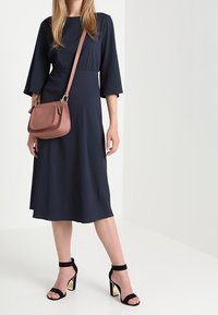 Námořnické midi šaty s tříčtvrtečními rukávy, strukturovaná látka, ve spojení s růžovou přes rameno taškou a černými sandály na vysokém podpatku se zlatými akcenty.