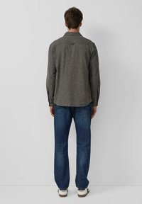 Grijze textuur shirt met een kraag, lange mouwen en een gebogen zoom, gecombineerd met blauwe denim jeans en witte sneakers. Achteraanzicht.