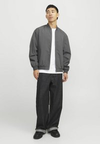 Gray bomber jacket with a ribbed collar and cuffs, paired with loose-fitting dark denim pants and black shoes. Simple and functional design.