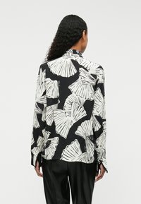 Camicia a maniche lunghe in tessuto bianco e nero con motivo floreale, dotata di colletto classico e polsini con bottoni.