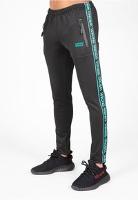 Zwarte sportieve joggers met ritszakken, turquoise zijstrepen en logodetail. Textuurstof met een taps toelopende pasvorm.
