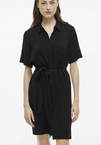 Juodas mygtukais užsegamas suknelė, pagaminta iš tekstūruoto audinio, su trumpomis rankovėmis, juosmens juosta ir krūtine kišene papildomam akcentui.