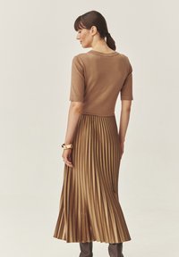 Top de punto marrón combinado con una falda midi plisada en un tono similar. Textura suave con una silueta fluida y mangas cortas.