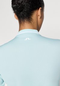 Top atlético azul claro com um tecido texturizado, apresentando uma gola canelada e um pequeno logotipo branco na parte de trás.