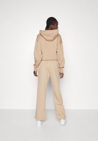 Sudadera recortada beige con una gran capucha, combinada con pantalones de chándal de pierna ancha a juego. Fabricada en tejido suave, diseño minimalista. Incluye zapatillas blancas.