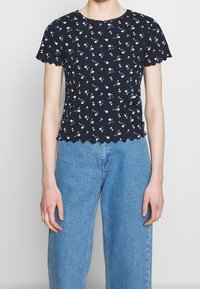 T-shirt navy con stampa floreale, a maniche corte e bordi ondulati, caratterizzato da piccoli fiori bianchi e foglie verdi, realizzato in morbido cotone.