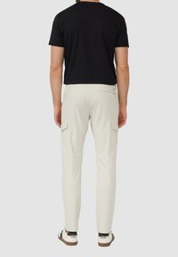 Lichtbeige cargobroek met zijzakken en een slim fit, gecombineerd met een aansluitend zwart t-shirt en witte sneakers met bruine accenten.