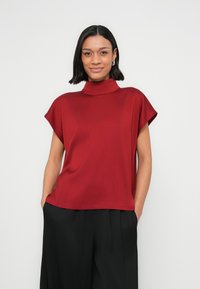 Czerwony top z golfem, krótkimi rękawami, gładką teksturą i luźnym krojem, zestawiony z czarnymi szerokimi spodniami.