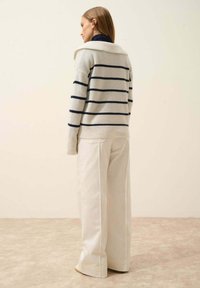 Randig tröja i krämfärgad med marinblå ränder, med en bred krage, ihop med vida vita byxor. Mjuk textur, avslappnad design.