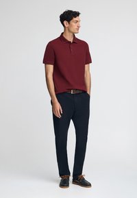 Bordeaux kortärmad polotröja med en traditionell krage, i kombination med marinblå byxor och mörka skor med orange snörning.