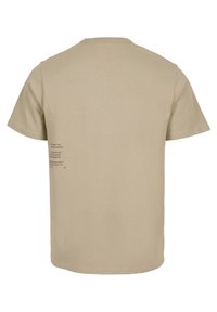 Camiseta de manga corta beige vista desde atrás, con pequeño texto impreso en negro cerca de la costura lateral izquierda.