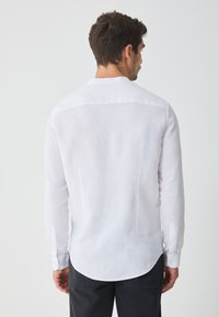 Witte linnen blouse met lange mouwen, klassieke kraag en gebogen zoom. Kenmerkt zich door knoopaccenten op de manchetten en een lichte, gestructureerde stof.