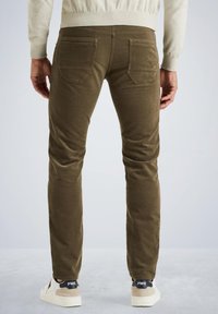 Oliwkowe skinny jeans z pięcioma kieszeniami i teksturowanym materiałem. Noszone z białymi trampkami z czarnymi i białymi akcentami.