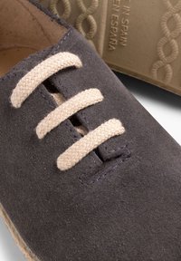 Scarpa in tessuto grigio scuro con lacci beige, caratterizzata da una superficie testurizzata e una suola di colore chiaro. L'interno è foderato con un materiale morbido.