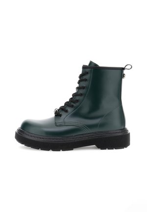 Green glossy ankle boot made of synthetic material, featuring black laces, a thick ridged sole, and a pull tab on the heel.