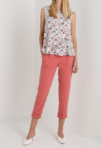 Bílé květinové bezramínkové tričko s růžovými a modrými vzory, zkombinované s korálovými zkrácenými kalhotami. Model má na sobě bílé vysoké pantofle.